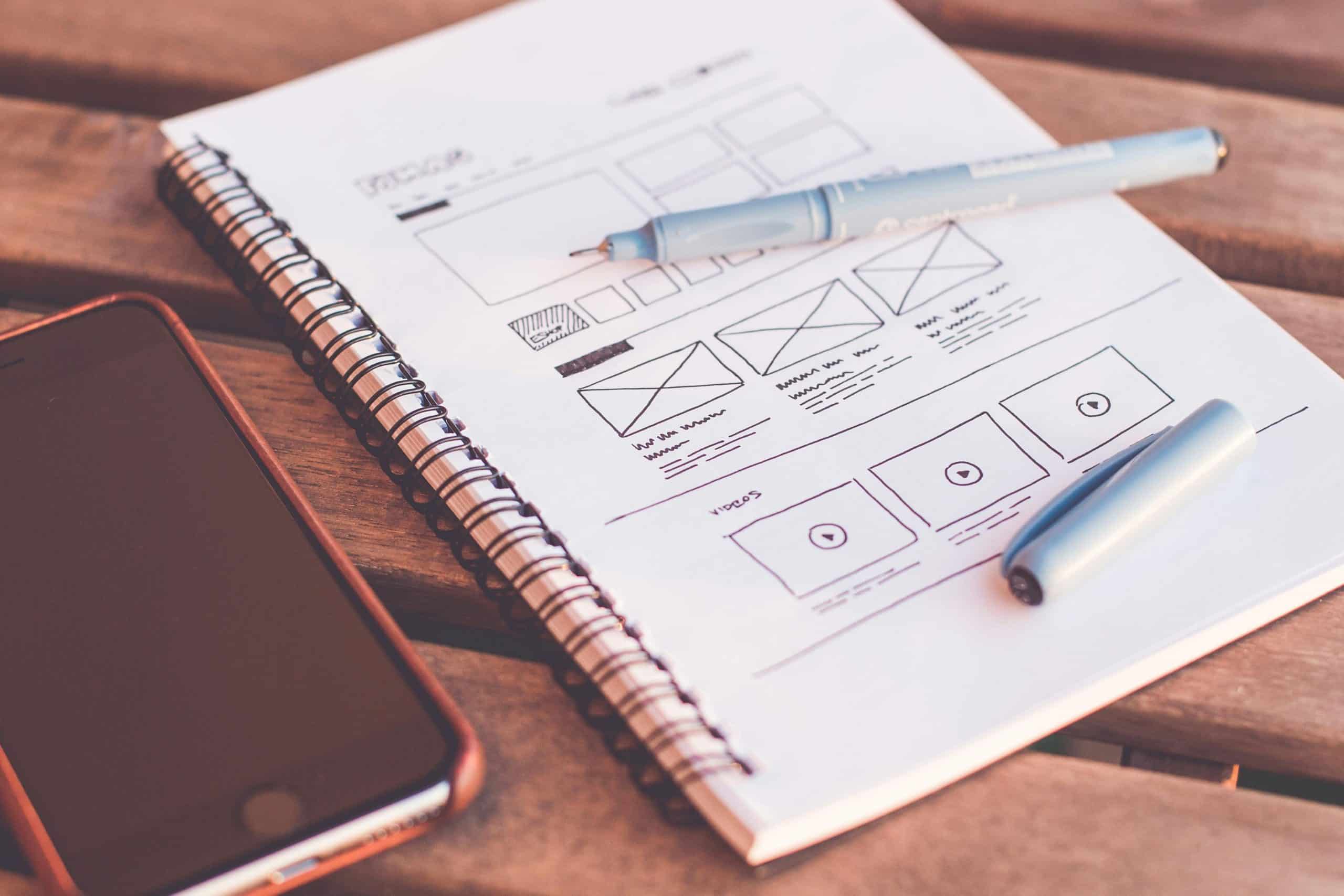 Notebook with website planning sketches, pen, and mobile phone on a desk